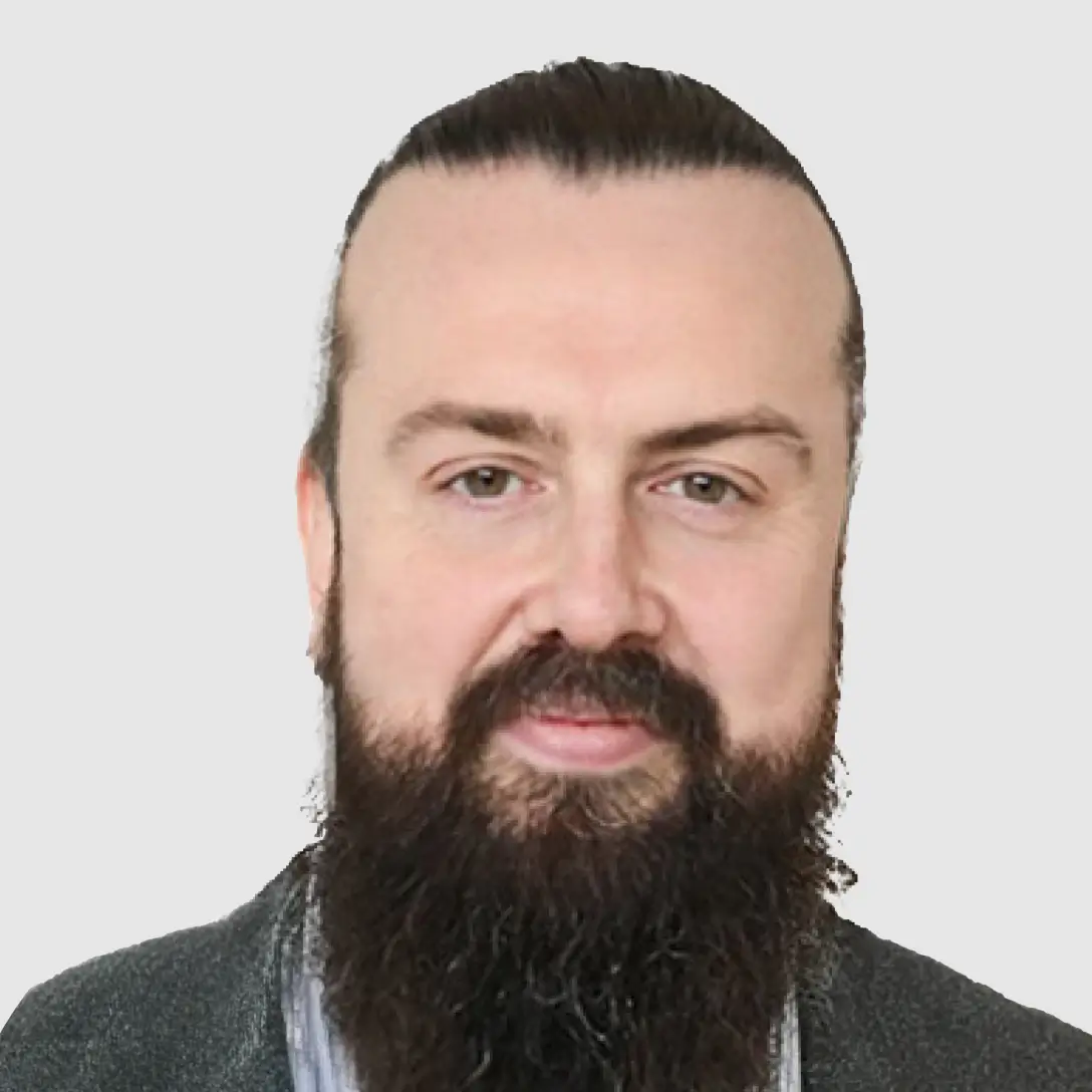 Portrait of a smiling woman with shoulder-length blonde hair, wearing a colorful beaded necklace, softly lit on a neutral gray background
